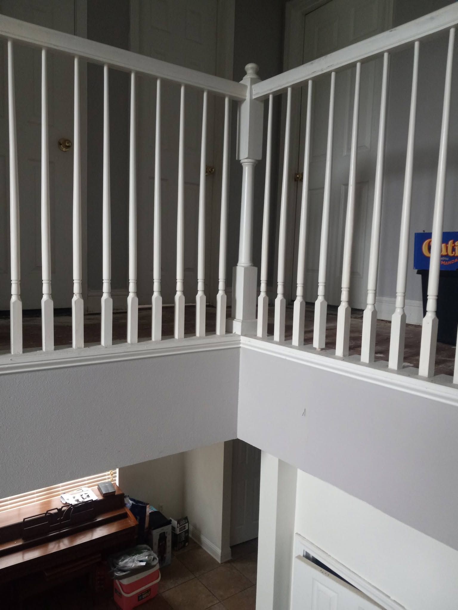 White railing on an indoor balcony overlooking a stairwell and lower level, with a wooden bench below.