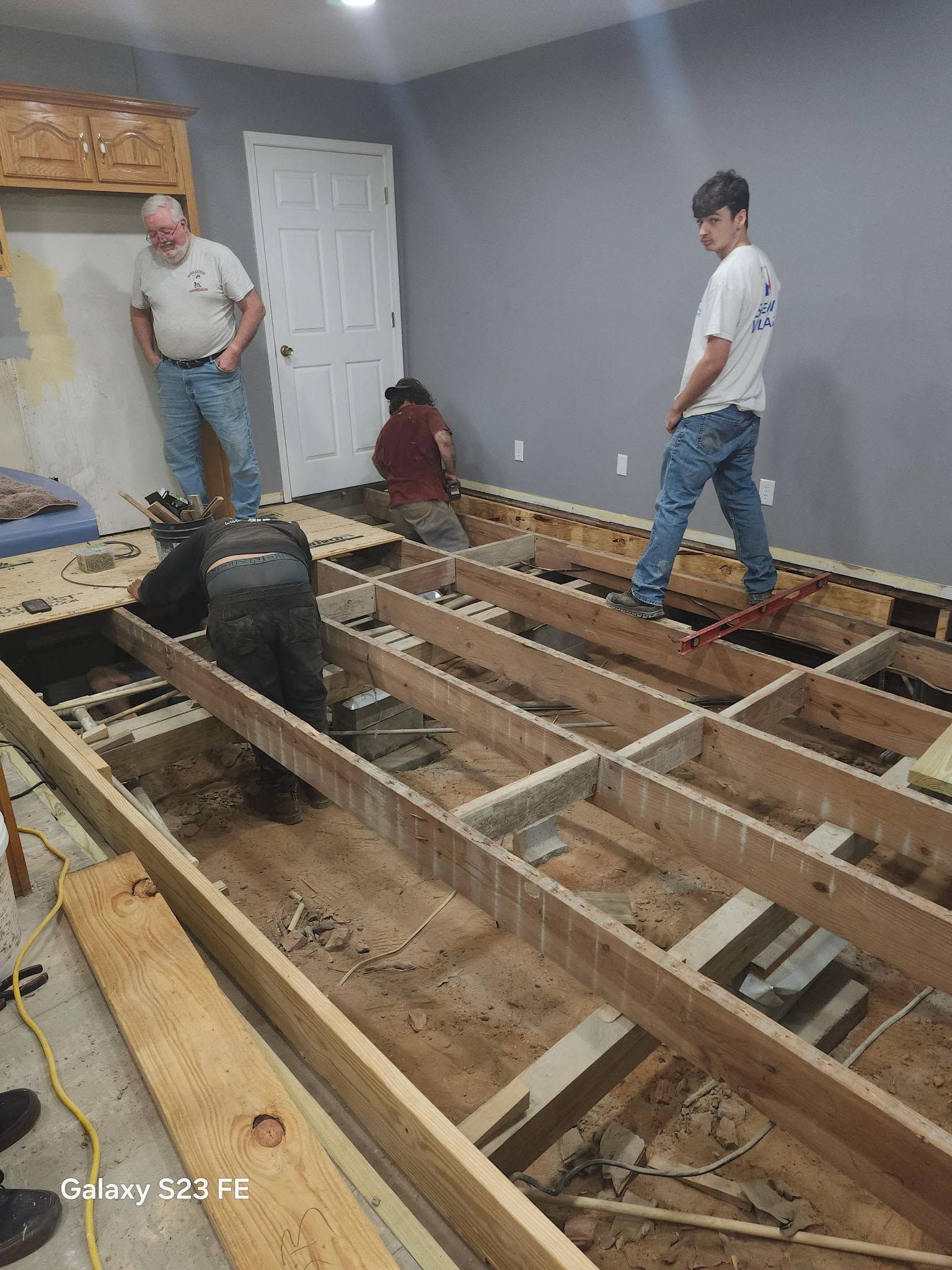 Two workers in a room with exposed floor joists during home renovation