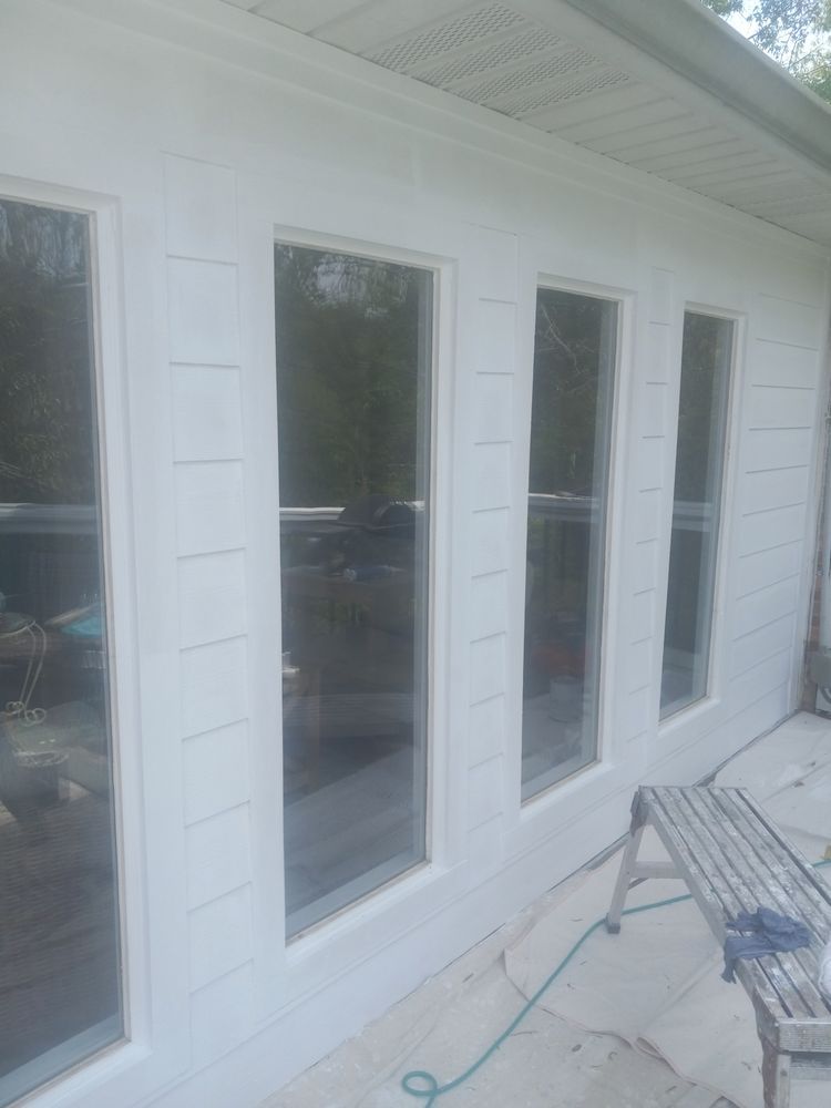 White exterior wall with several tall windows and a patio chair on a screened porch