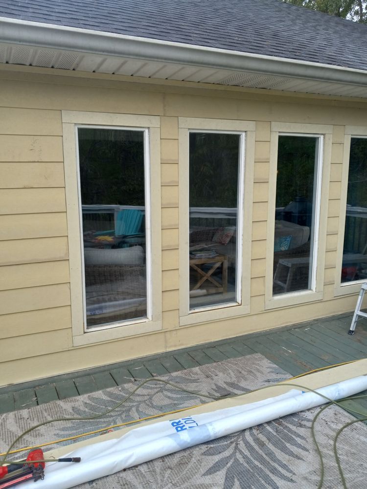 Exterior of a beige house with three tall windows and a patio door, with construction materials in the foreground
