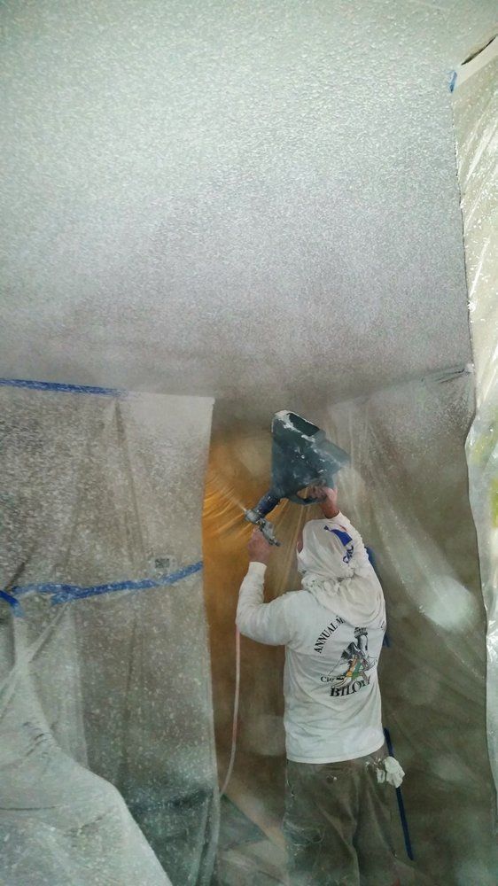 Worker spraying a white ceiling in a room covered with protective plastic sheeting