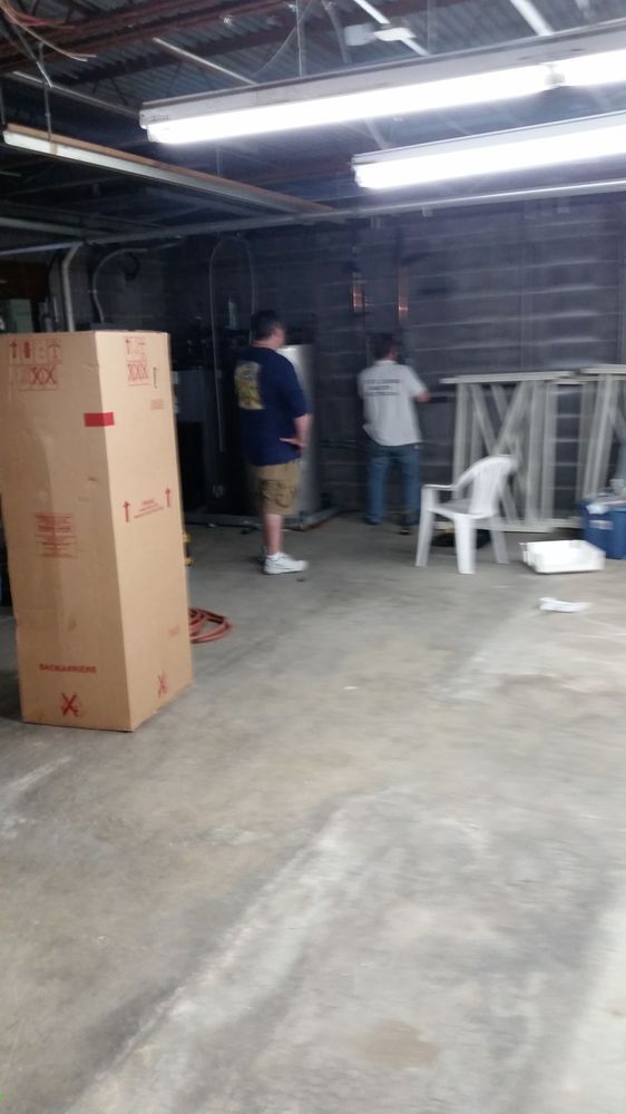Two people in a dim garage with stacked boxes, chairs, and exposed ceiling lights.