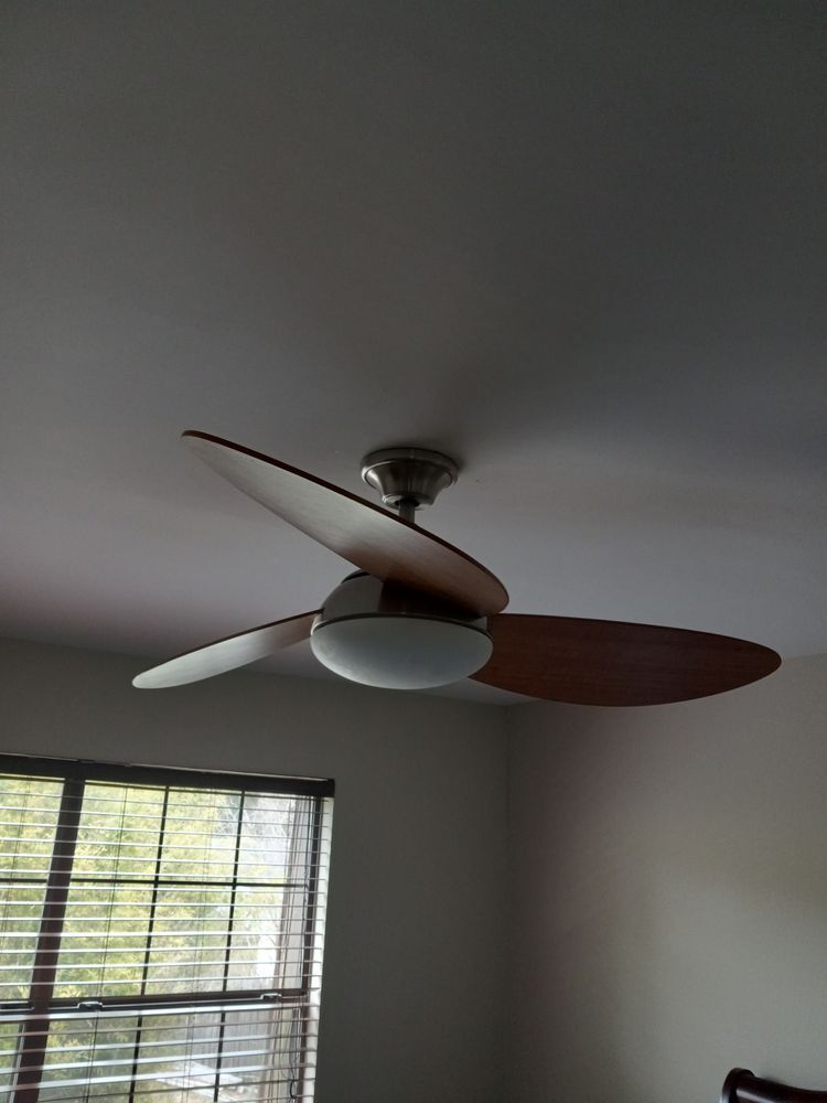 Ceiling fan with wooden blades in a room, above a window with blinds