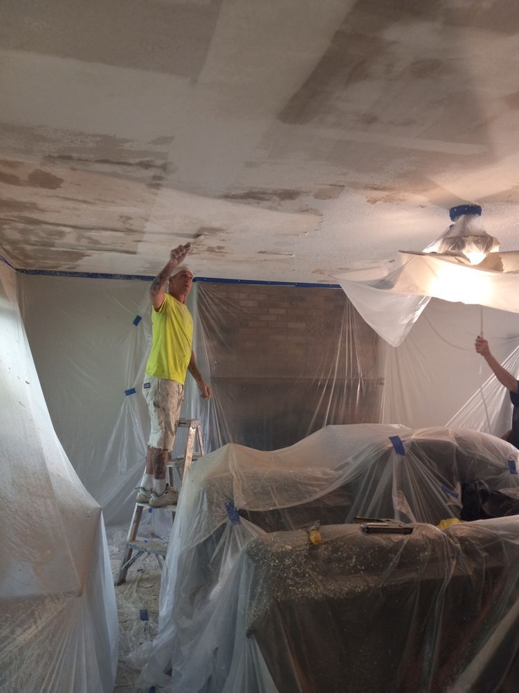 Two workers covering furniture with plastic sheeting while painting a room ceiling.
