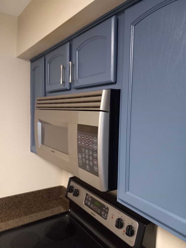 Blue kitchen cabinets above a stainless steel microwave and stove with a speckled countertop.