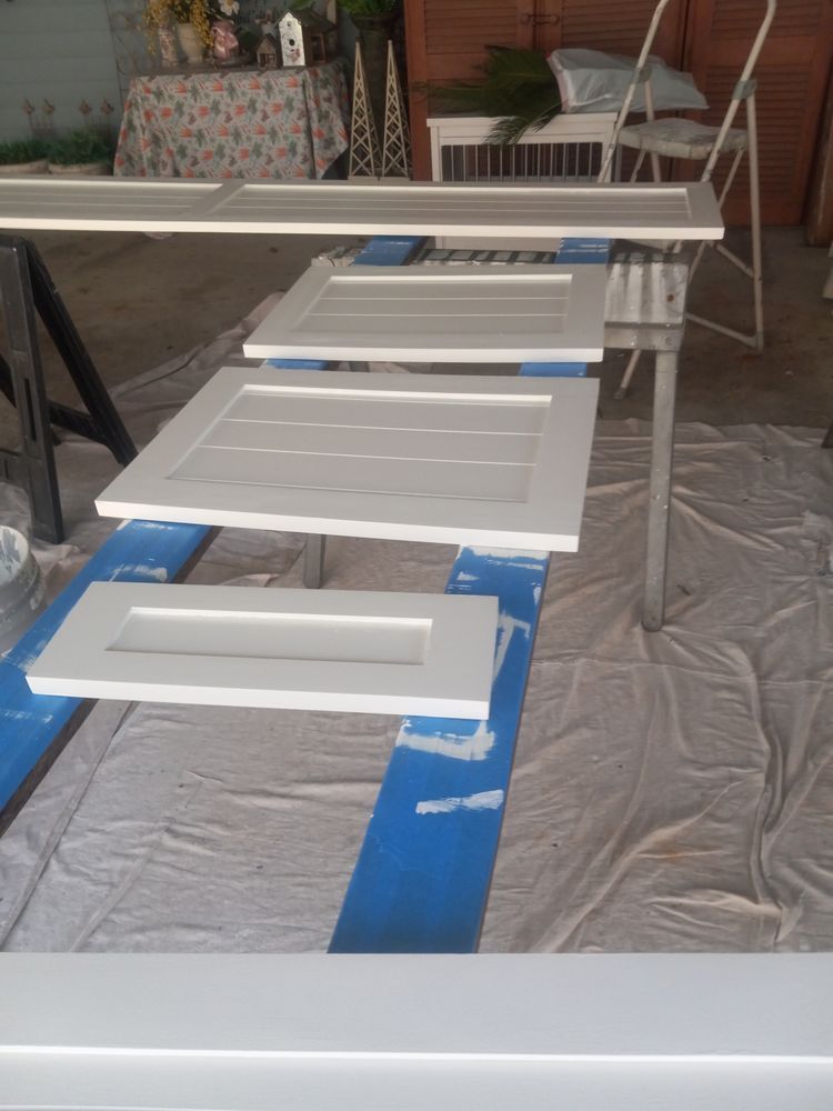 White doors being painted on a tarp-covered floor in a workshop or garage