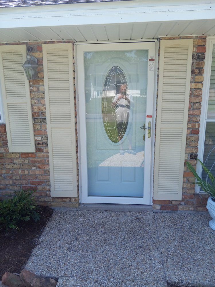 Front door with frosted glass oval insert, cream shutters, and brick exterior facade.