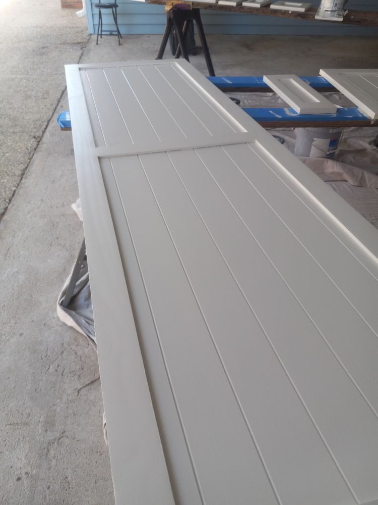 Long white panel resting on a blue workbench in a workshop, with concrete floor and tools nearby