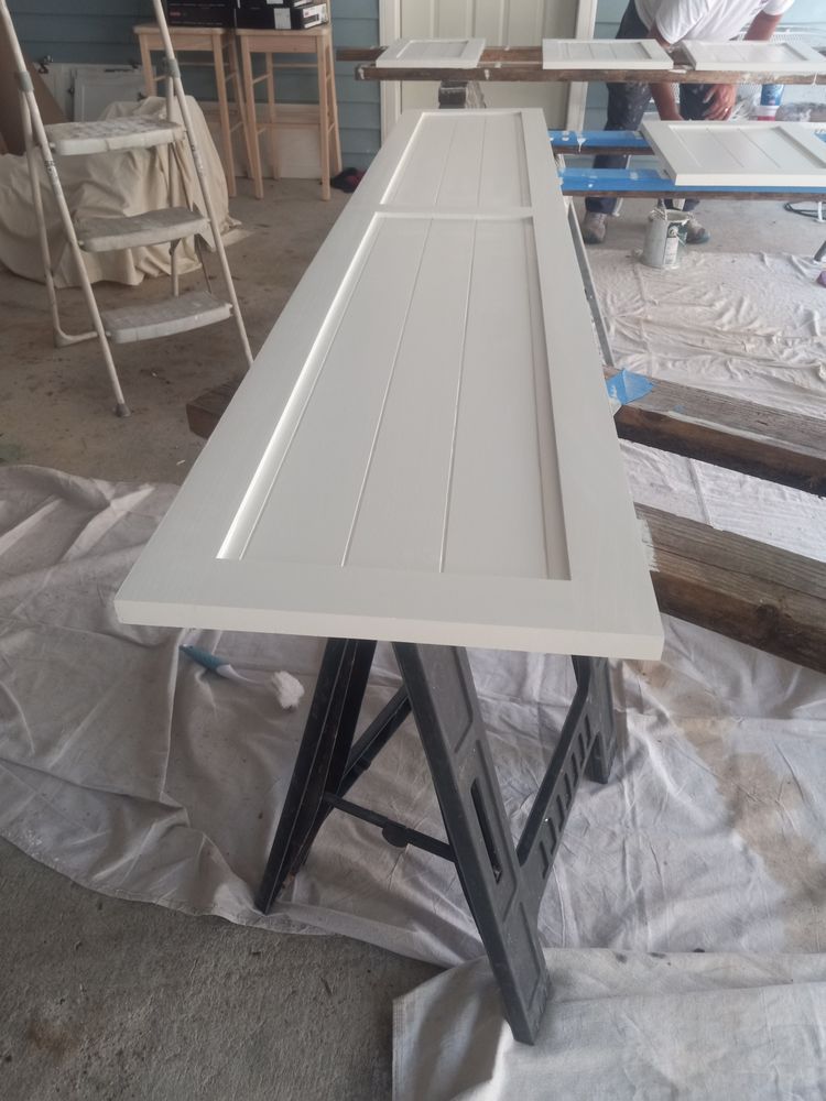 White cabinet door panel drying on a black sawhorse in a workshop.