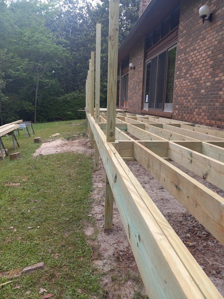 Partially built wooden deck beside a brick house, with upright posts and framing in a grassy yard