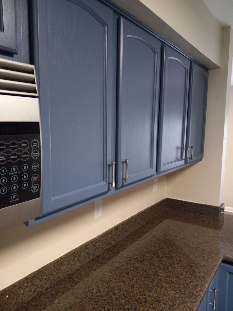 Blue kitchen cabinets above a brown speckled countertop and microwave area