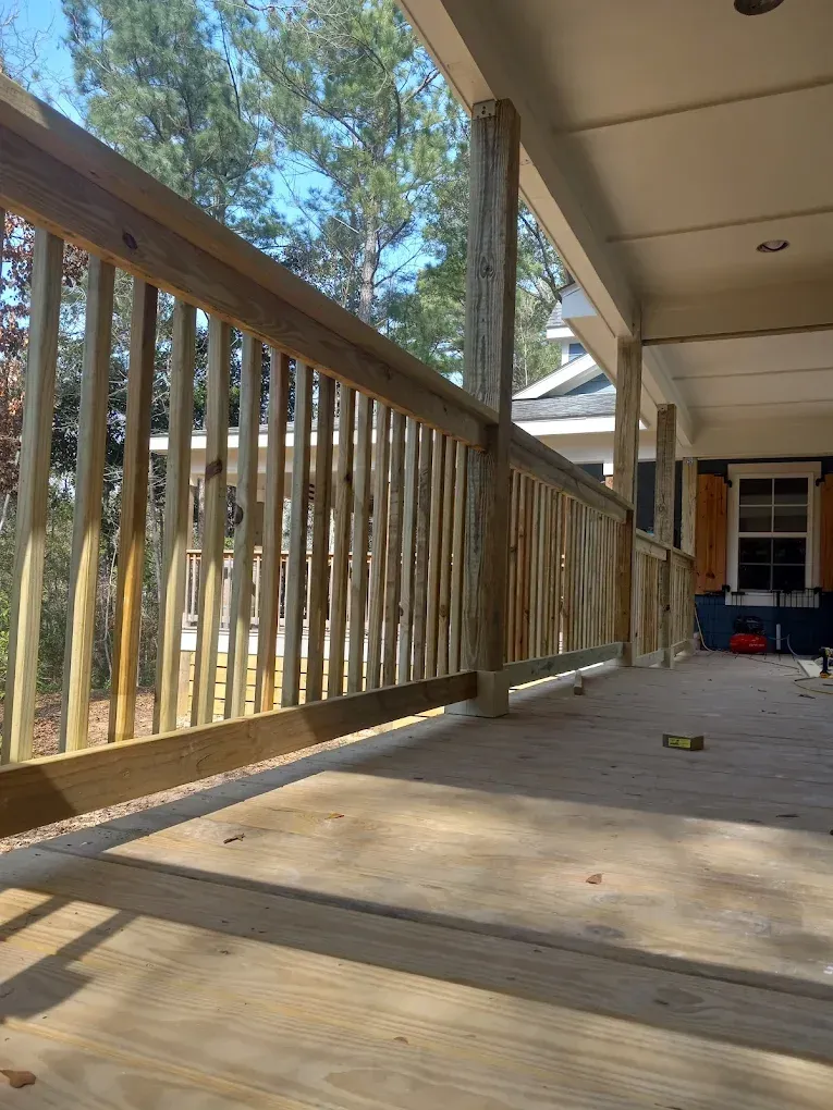 Wooden porch with railing, sunlit trees, and a front door in the background