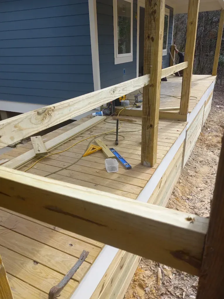 Partially built wooden porch beside a blue house, with tools and framing materials on the floor.