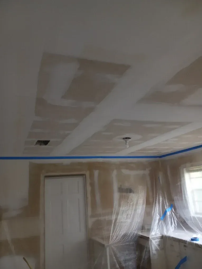 Partially finished room with drywall ceiling patches, taped walls, a door, and plastic-covered window area