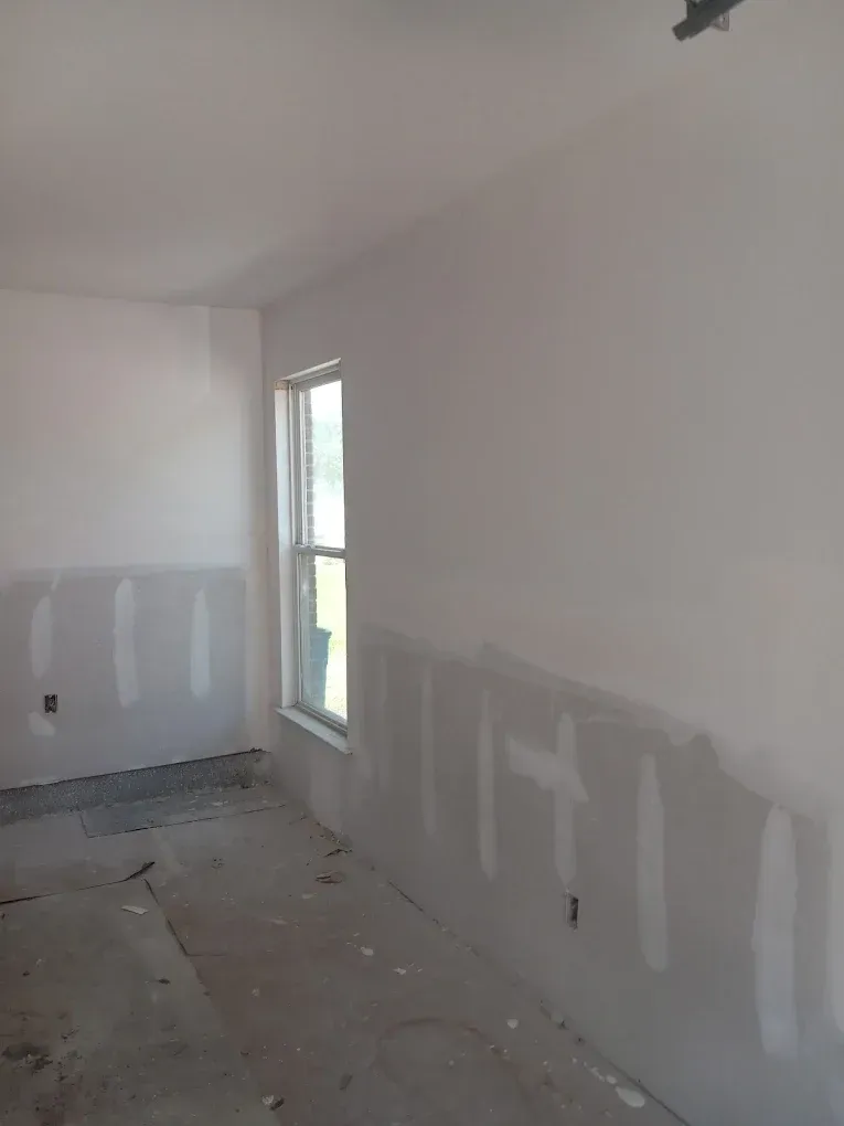 Bare room under renovation with white walls, patchy drywall, and a window on the right.