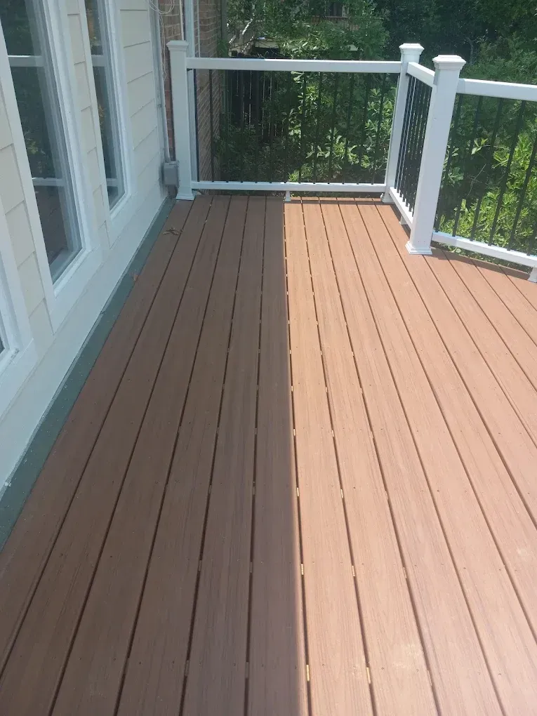 Wooden porch deck with brown and tan boards beside white siding and railing in sunlight