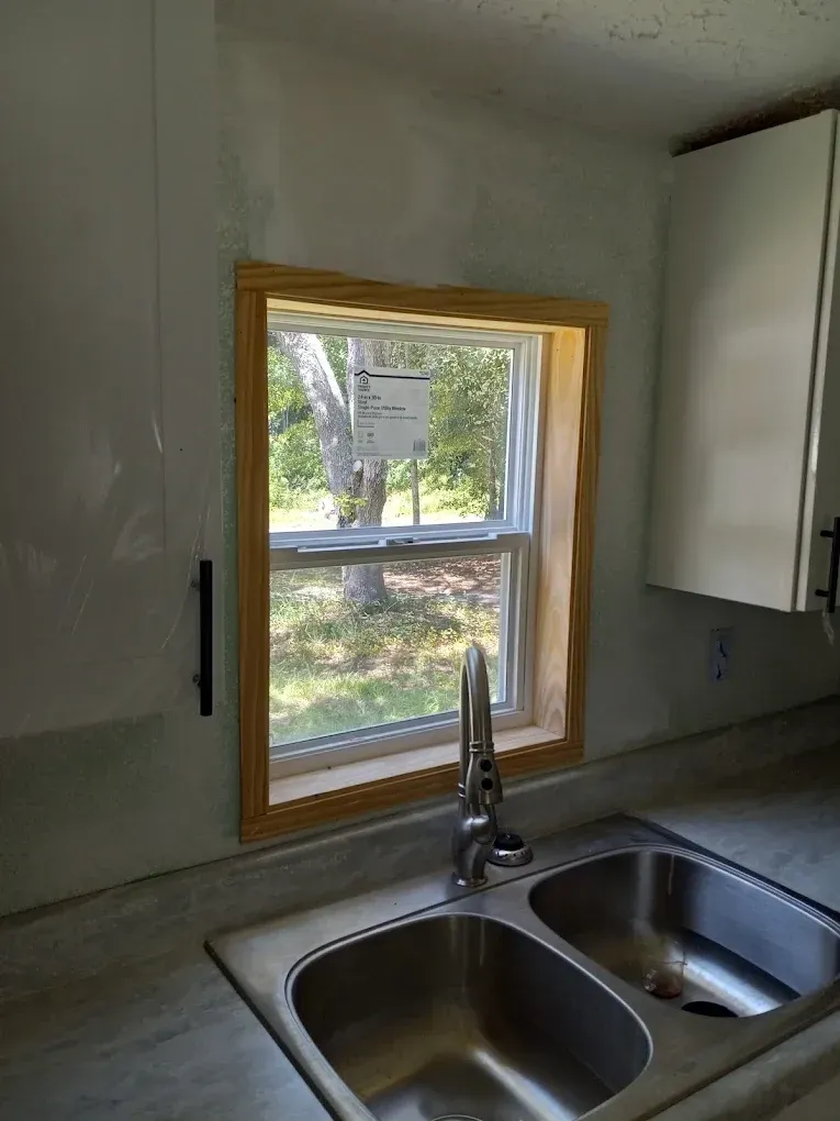 Kitchen sink beneath small window with white cabinets and a view of trees outside