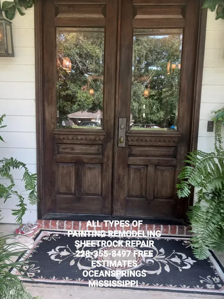 Dark wooden double doors on a white porch, with a black doormat and a tree reflected in the glass panes
