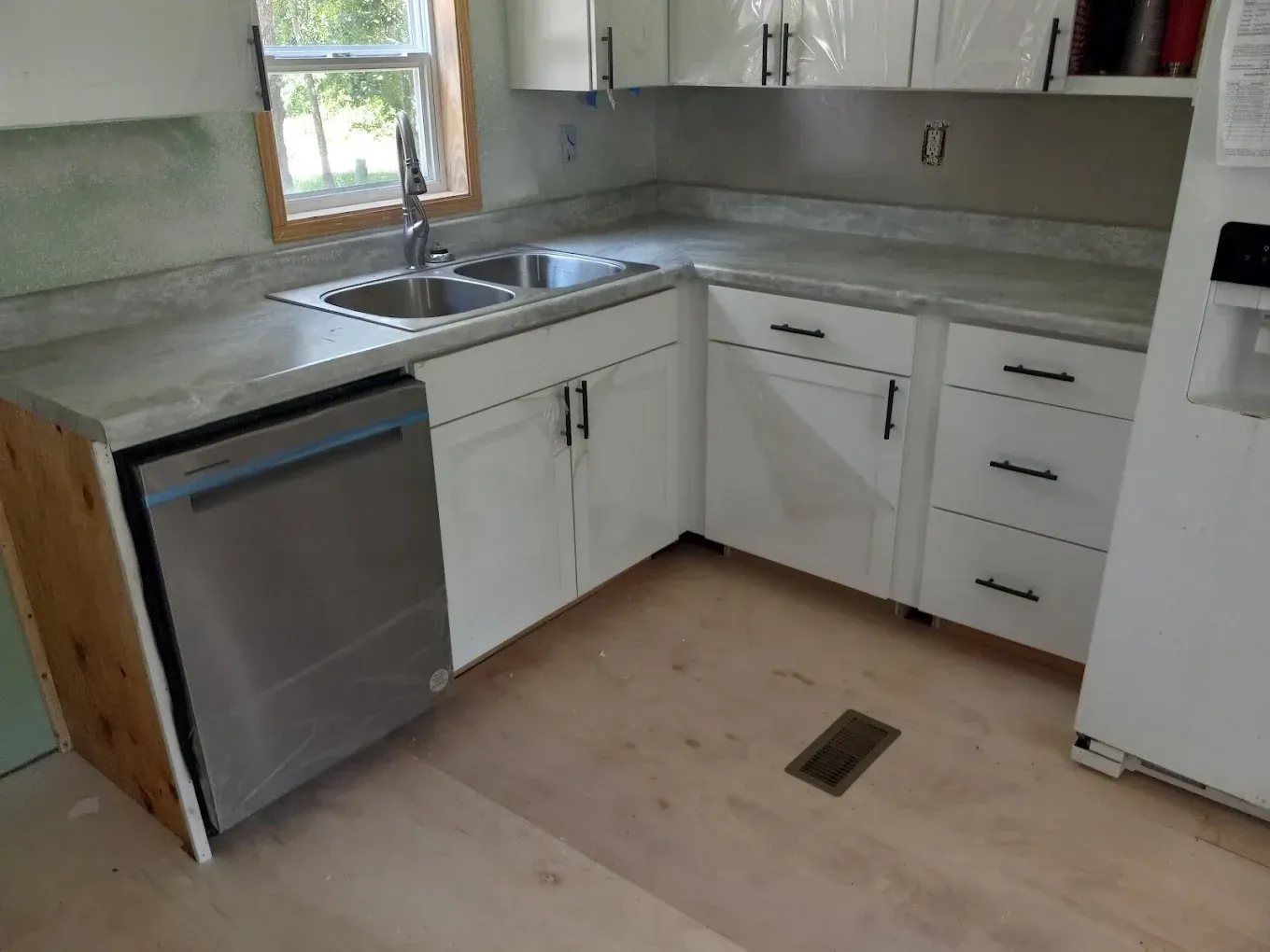 Small L-shaped kitchen with white cabinets, stainless dishwasher, sink by window, and light counters.