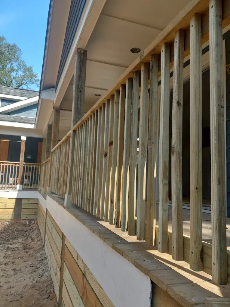 Wooden porch railing beside a beige house under construction, viewed along the deck edge