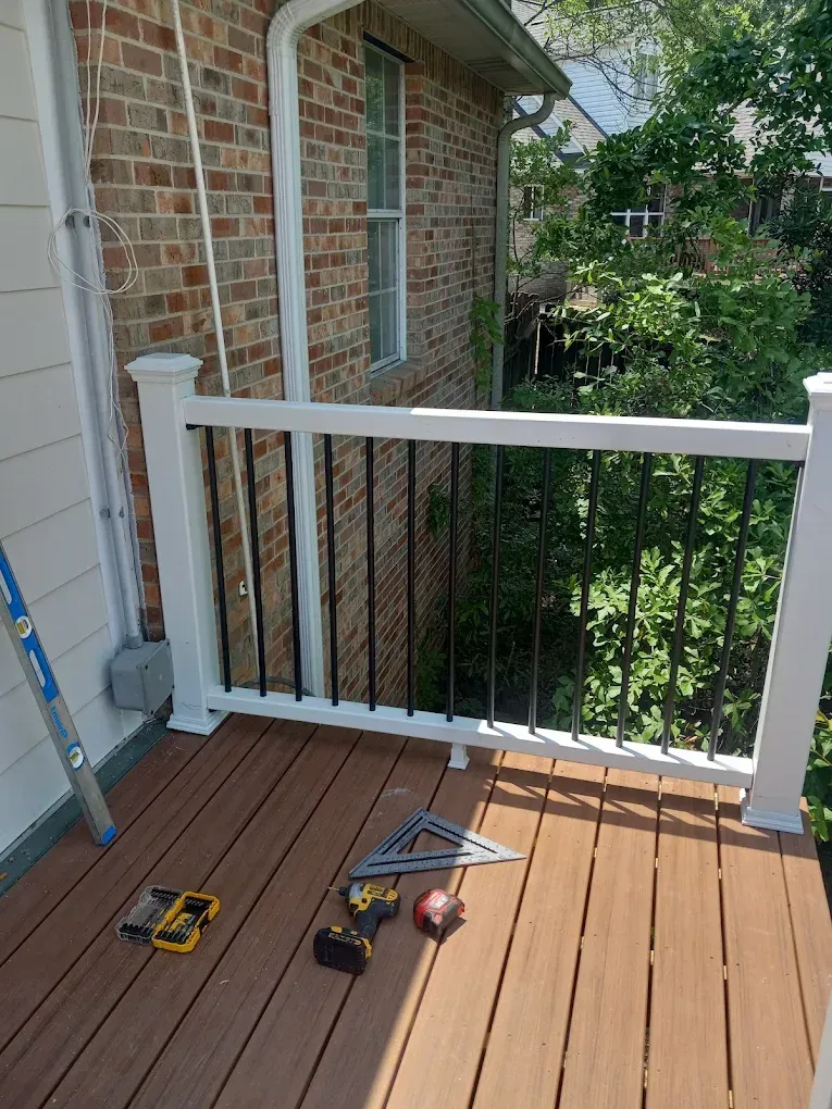 Small wooden balcony with white railing, brick wall, and tools on the floor during repairs