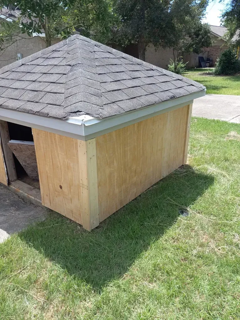 Wooden shed with a gray shingled roof on a grassy lawn outdoors