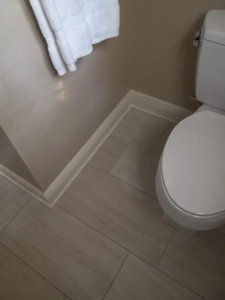 Corner of a beige bathroom with a toilet, white towel, and light wood-look tile flooring
