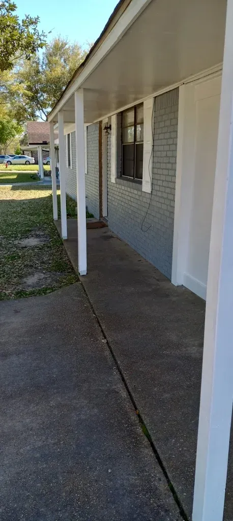 Covered apartment walkway with white columns, gray siding, and concrete path in daylight