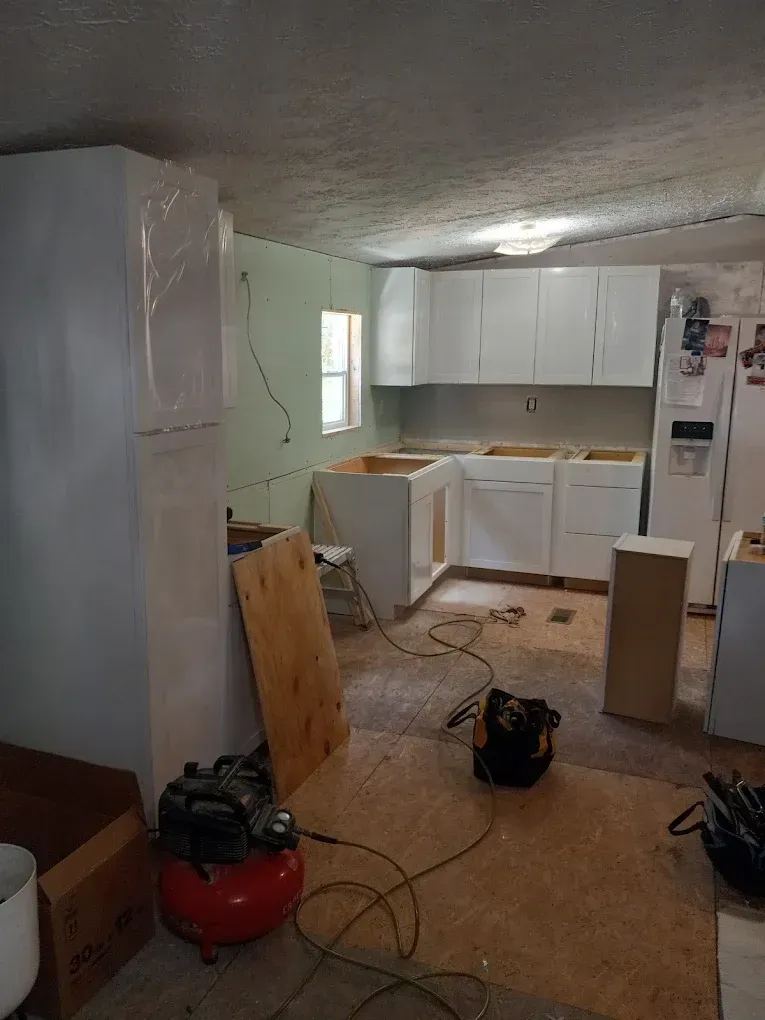 Unfinished kitchen with white cabinets, refrigerator, and tools scattered on the floor during renovation.