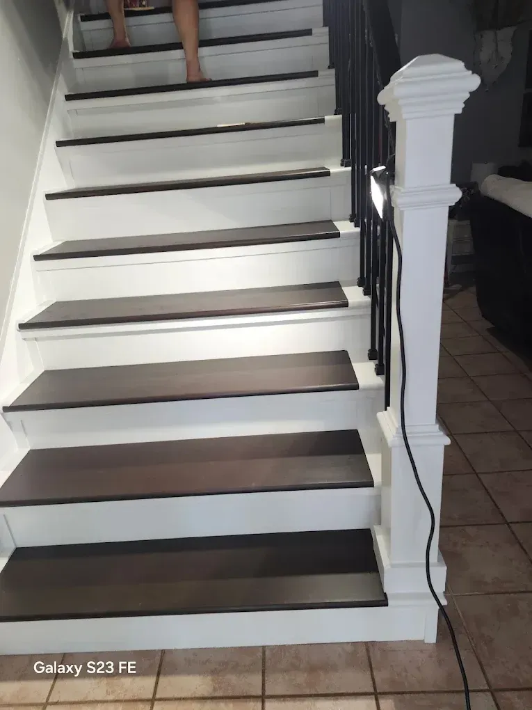 White staircase with dark treads and a lit railing in a tiled entryway