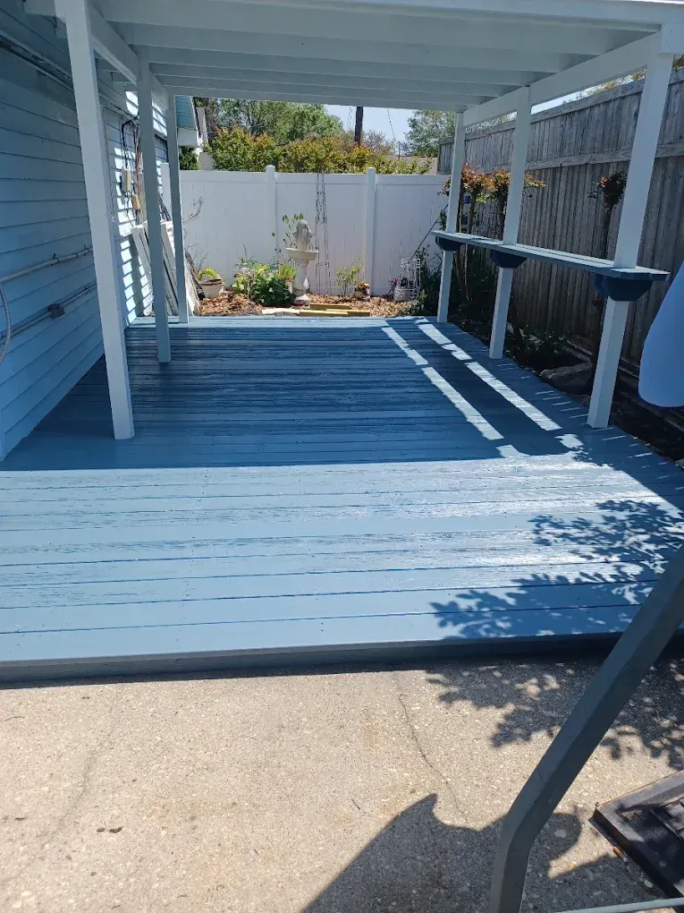 Covered backyard deck with blue siding, white railing, and a sunny walkway leading to a fenced garden.
