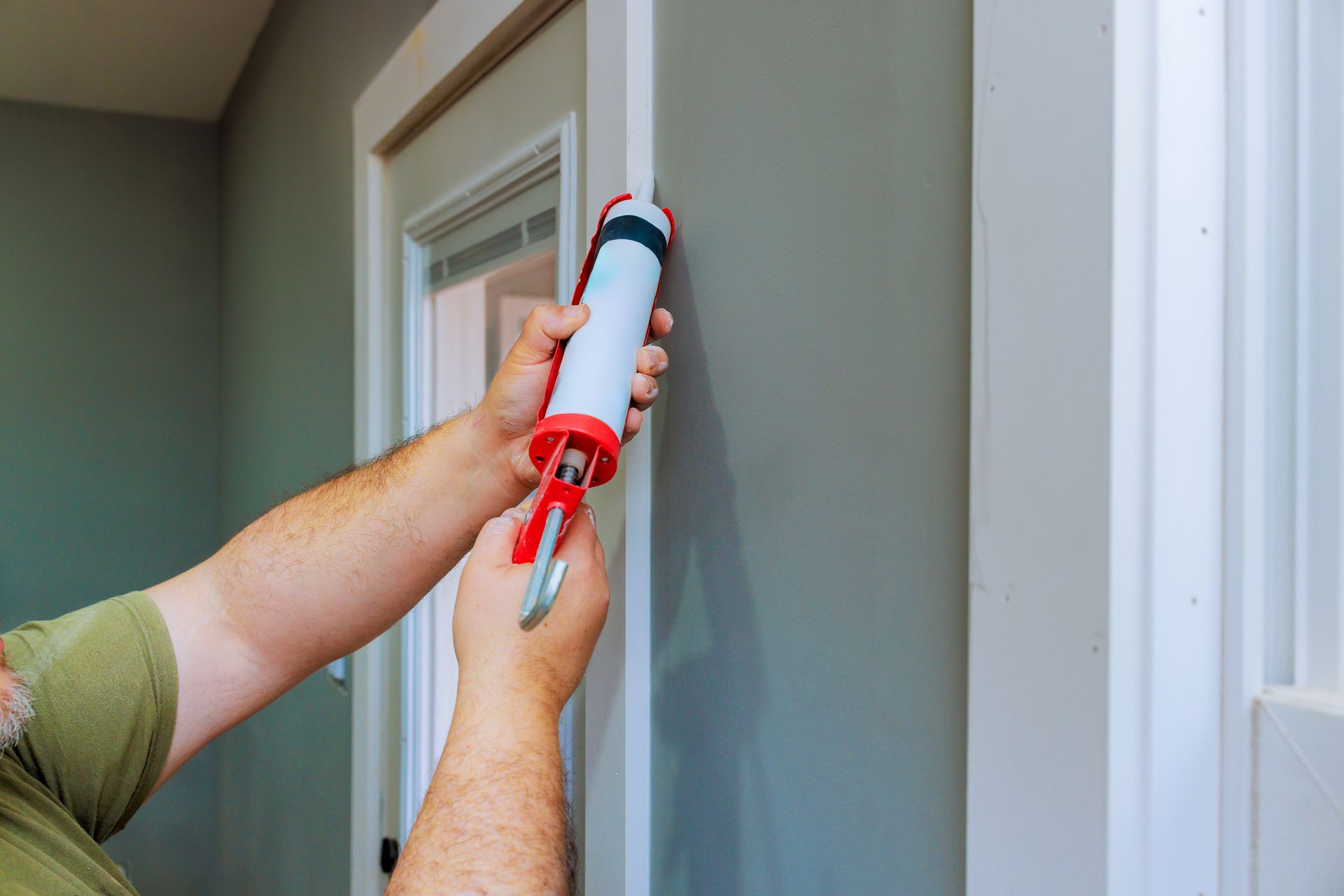 Person using caulk gun to seal trim around a door frame.