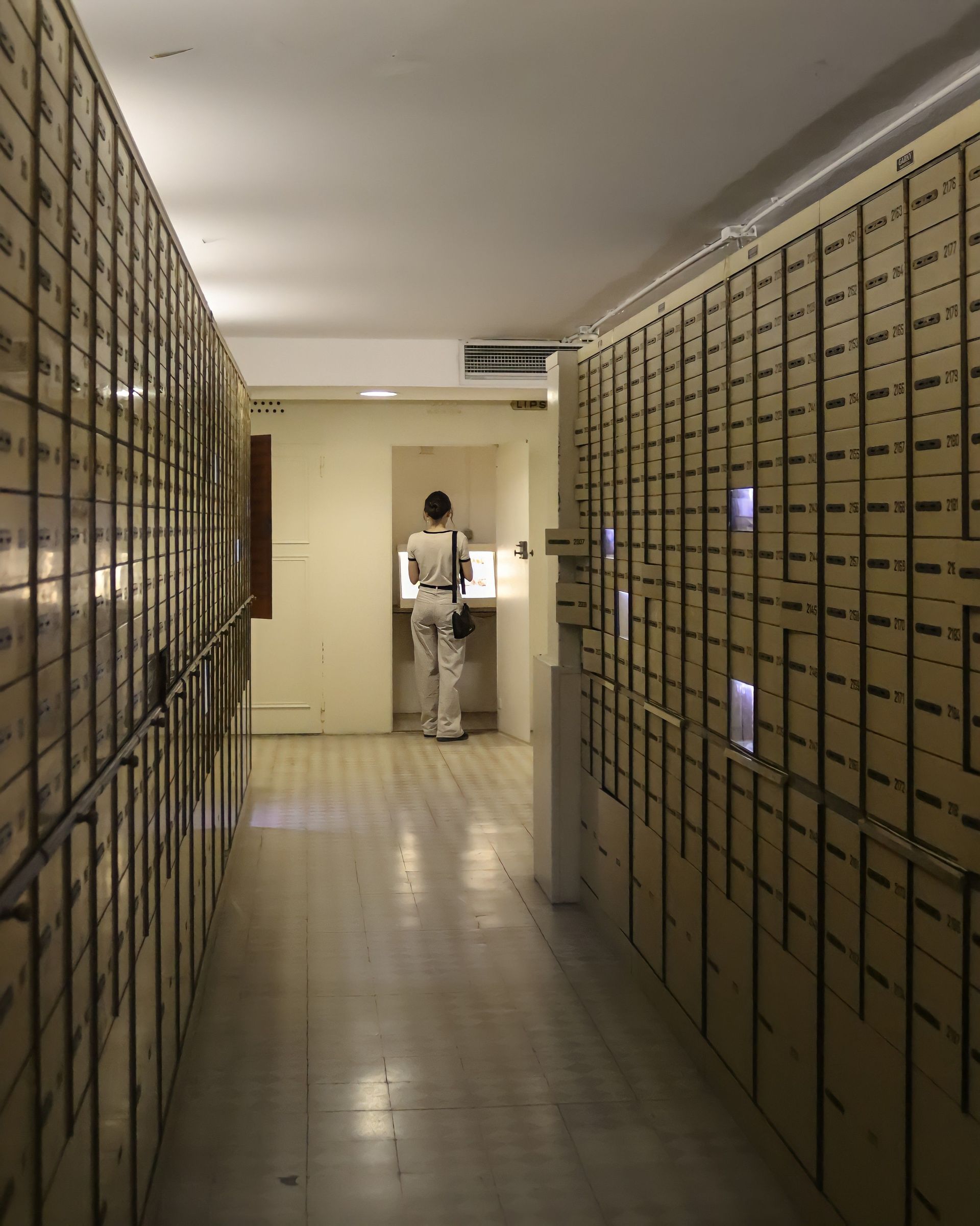 Narrow hallway lined with wall-to-wall mailboxes, with a person standing at a counter in the distance.
