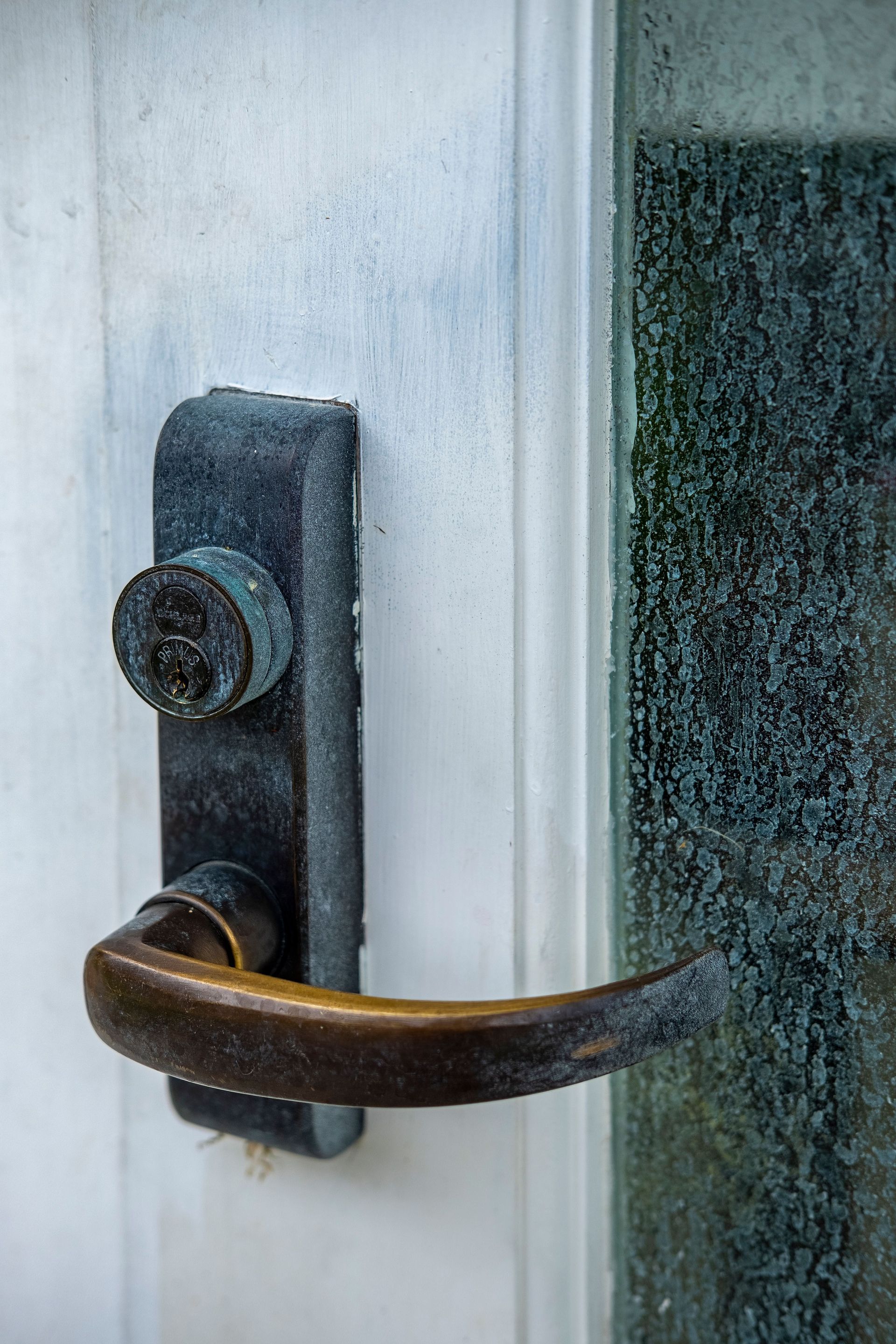 Close-up of a weathered dark metal door handle and lock on a white door frame