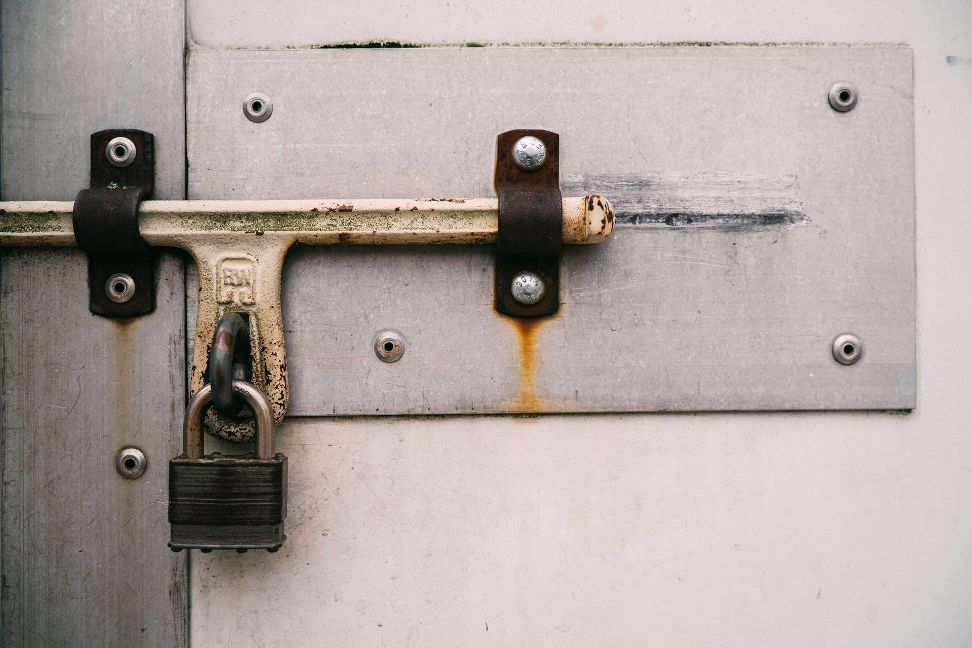 Rusty padlock on a metal sliding door latch with a silver plate.