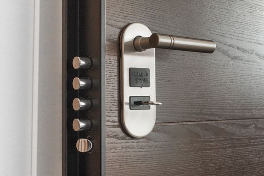 Close-up of a modern door lock with a metal handle and key inserted in a dark wood door