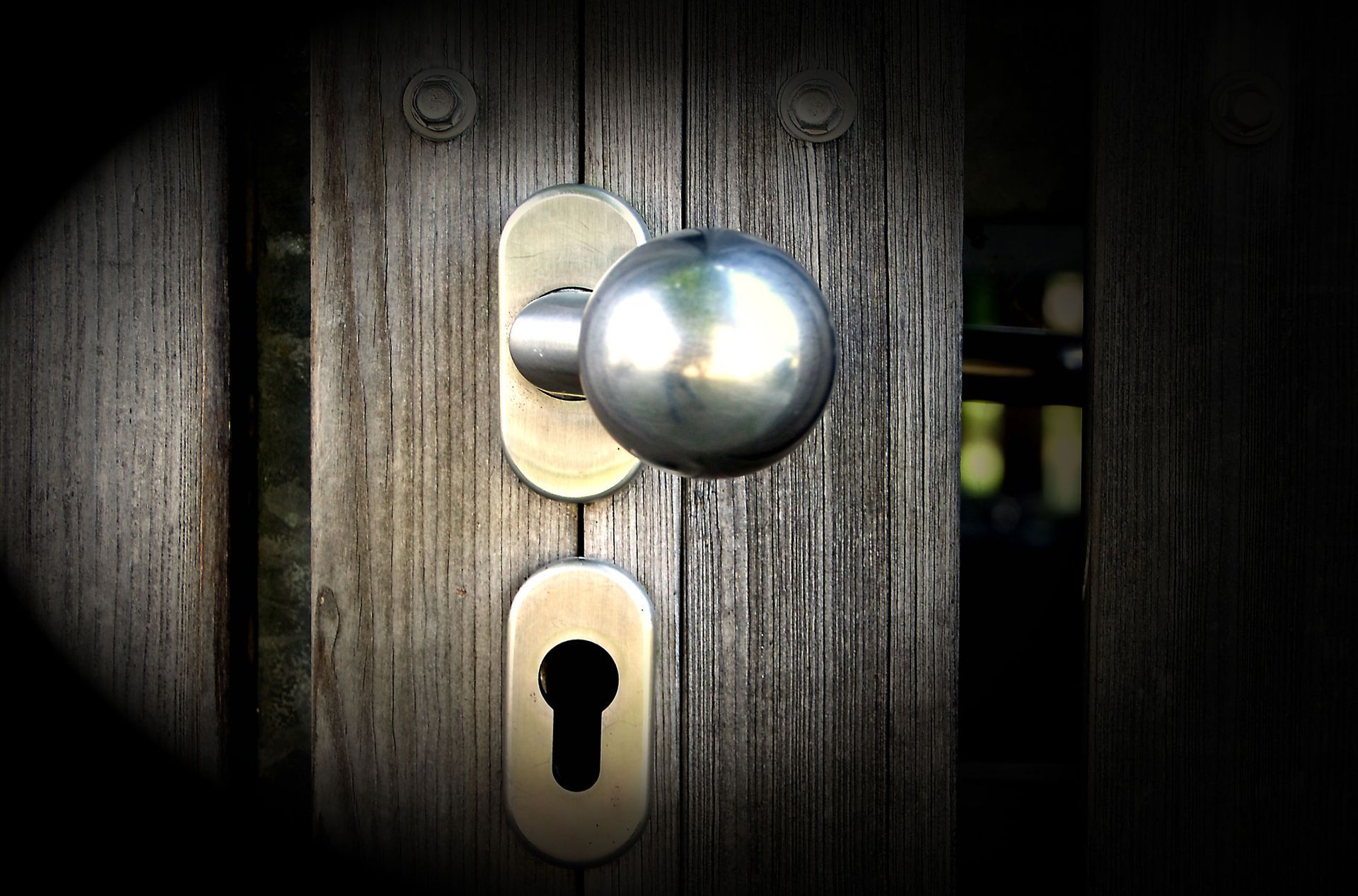Close-up of a silver door knob and keyhole on a weathered wooden door