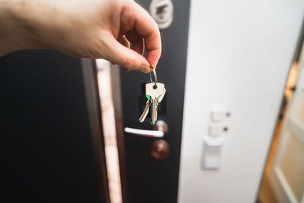 Hand holding a set of keys in front of a door lock and white wall switch