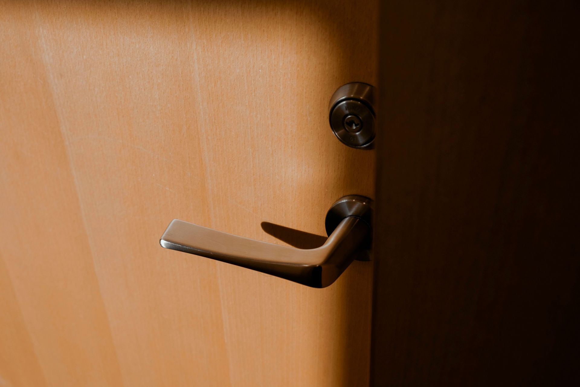 A silver door handle on a partially open wooden door, with warm light casting shadows.
