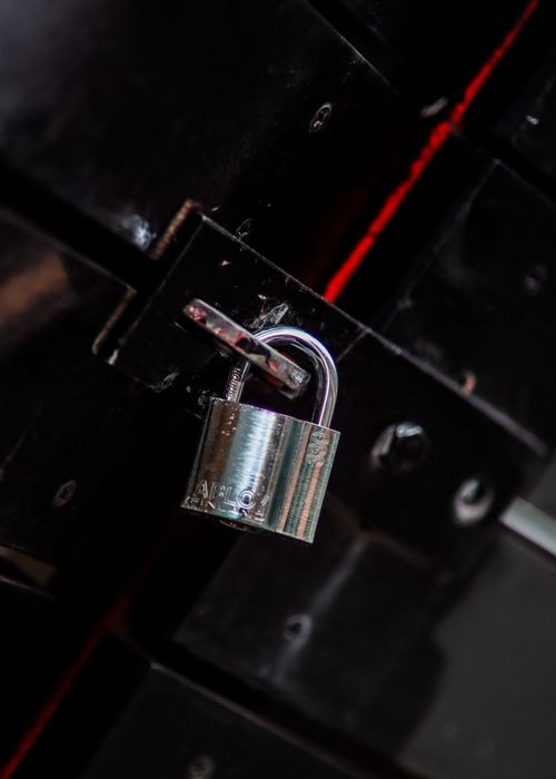 Open silver padlock hanging on a dark metal gate with a red stripe in the background