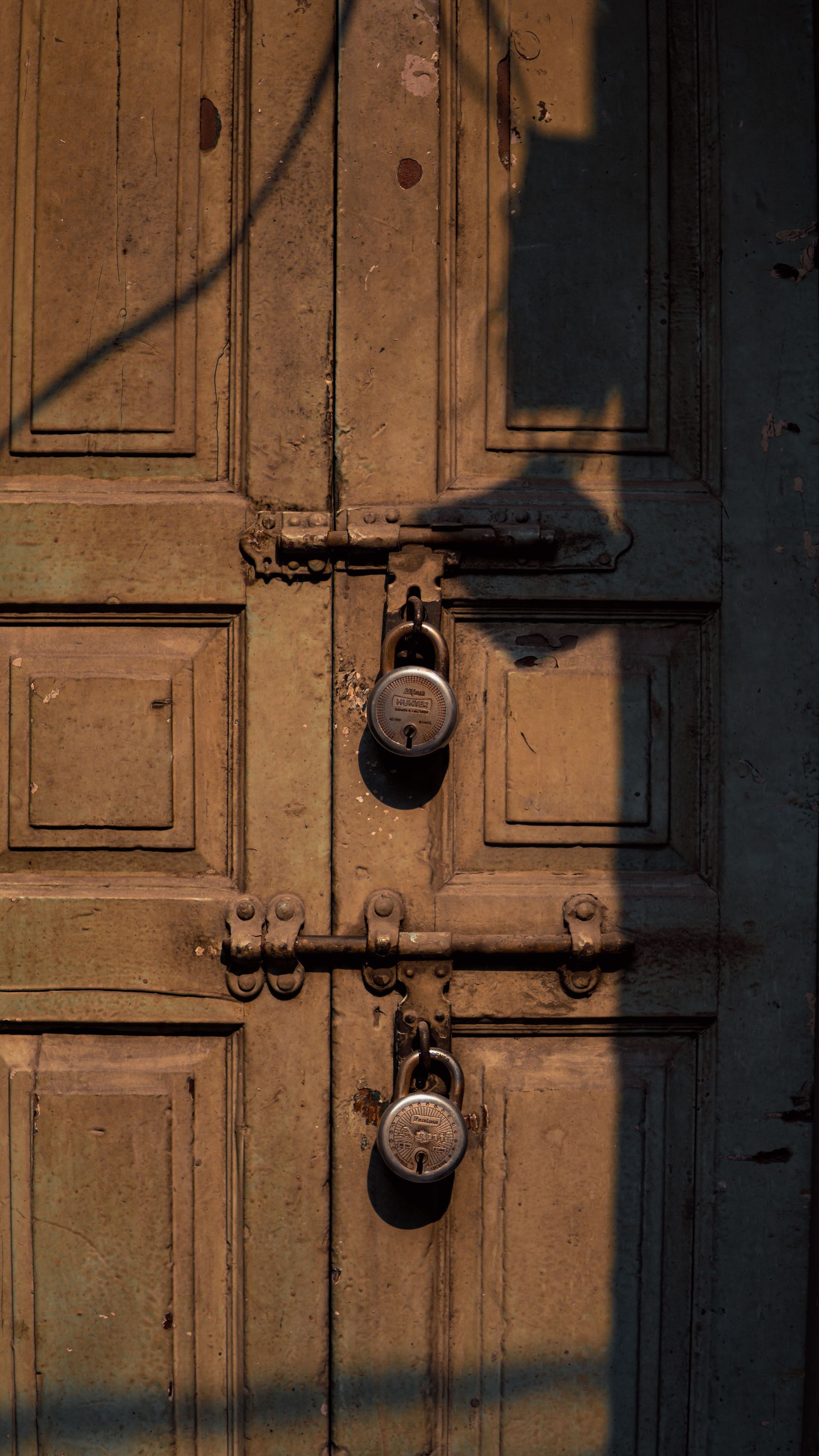 Sunlit wooden door with two ornate metal locks and deep shadow across the panels