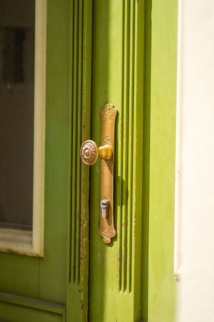 Close-up of a brass door handle on a green-painted door with vertical grooves.