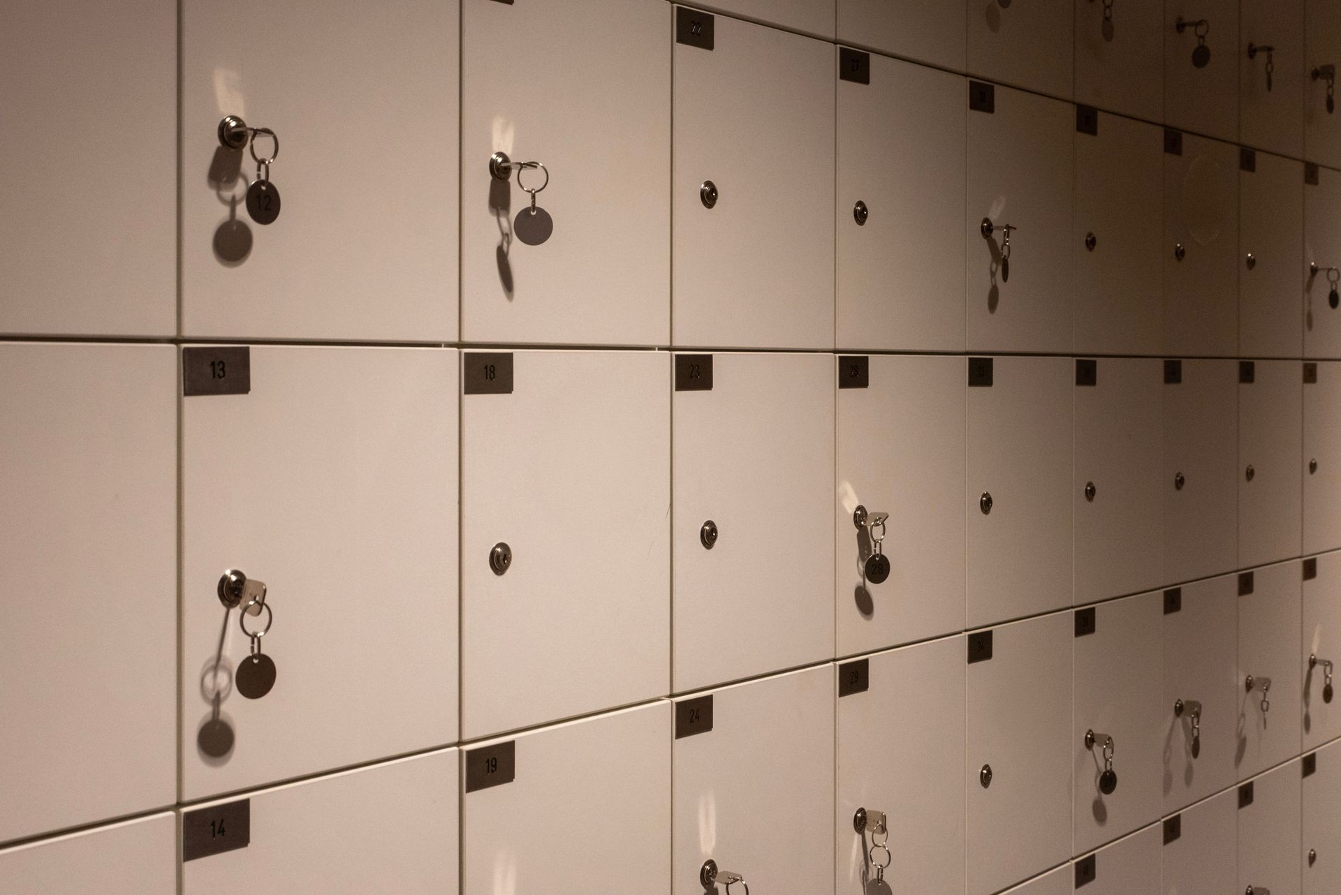 Rows of beige locker doors with black handles in a hallway.