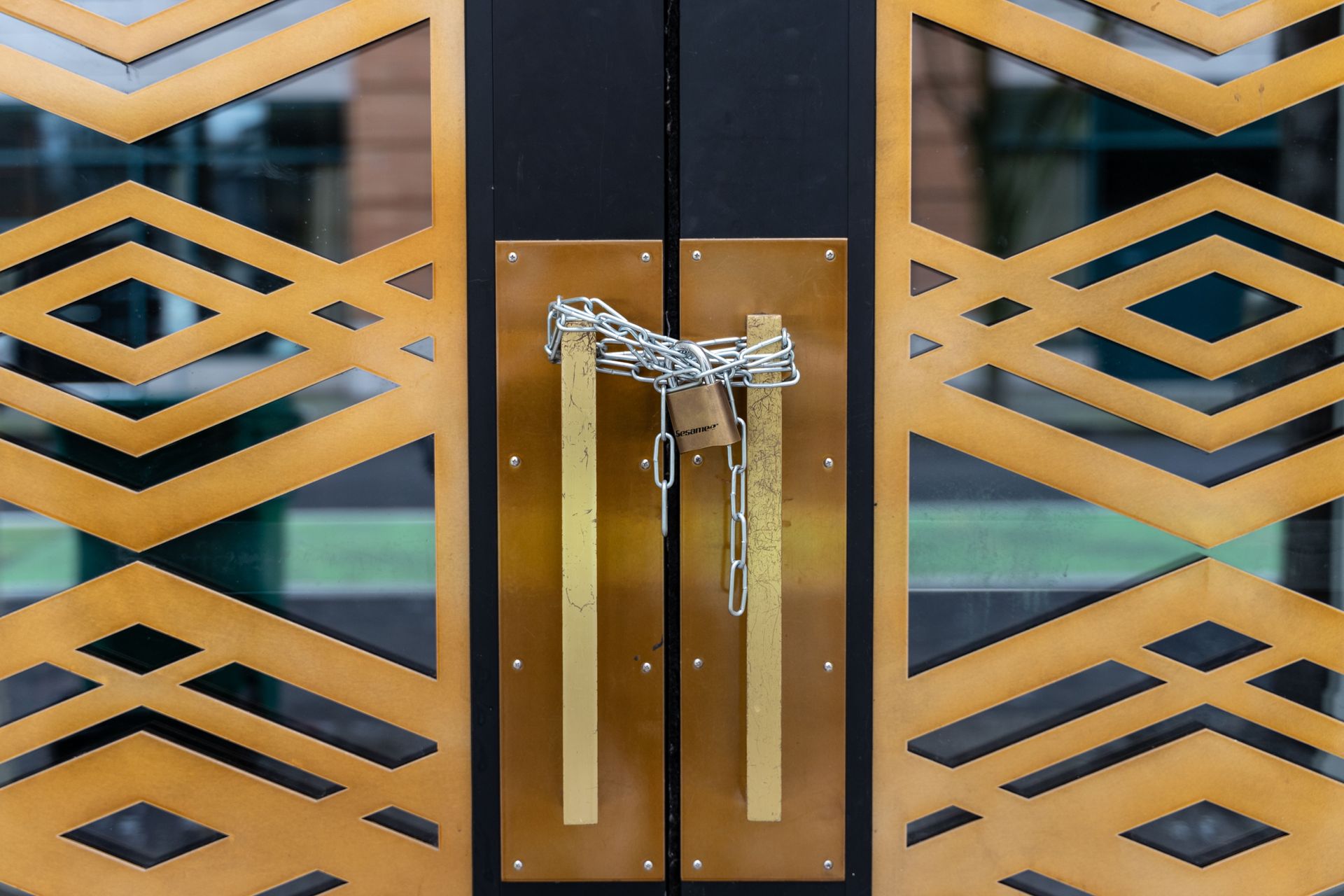 Closed glass door with gold geometric patterns and a central silver handle secured by a chain lock