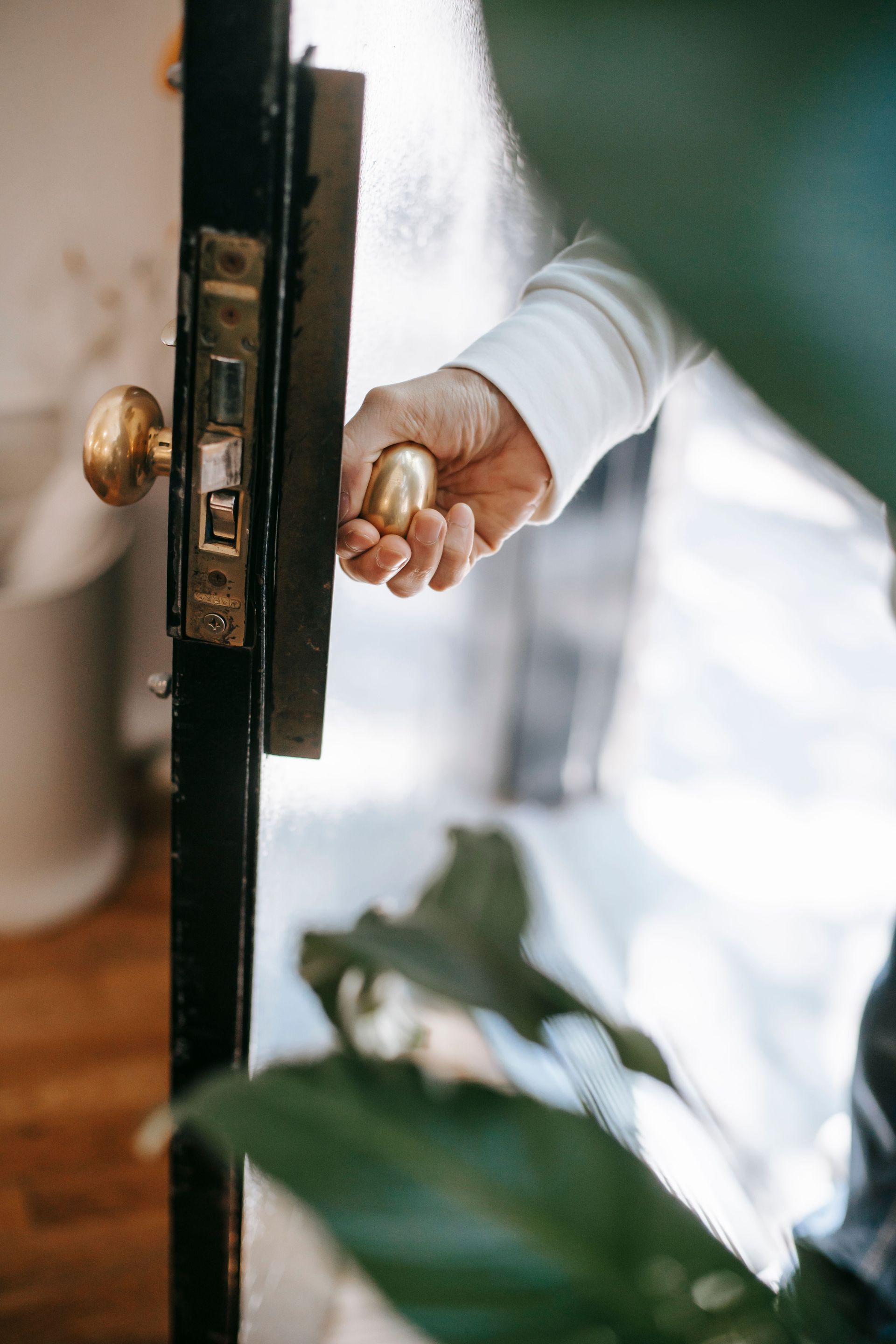 Hand opening a wooden door with a brass knob, viewed close up through the doorway