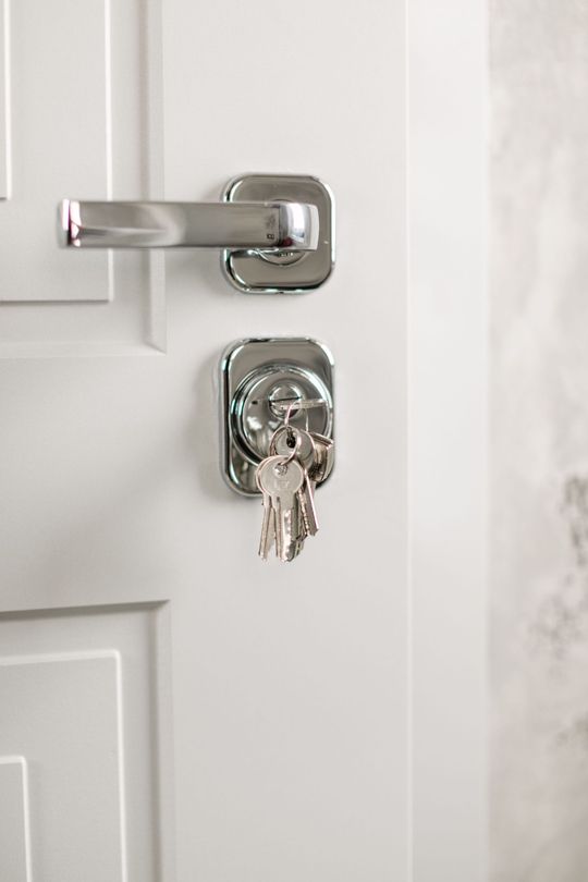 Close-up of a white door with a silver lock and key inserted in the deadbolt