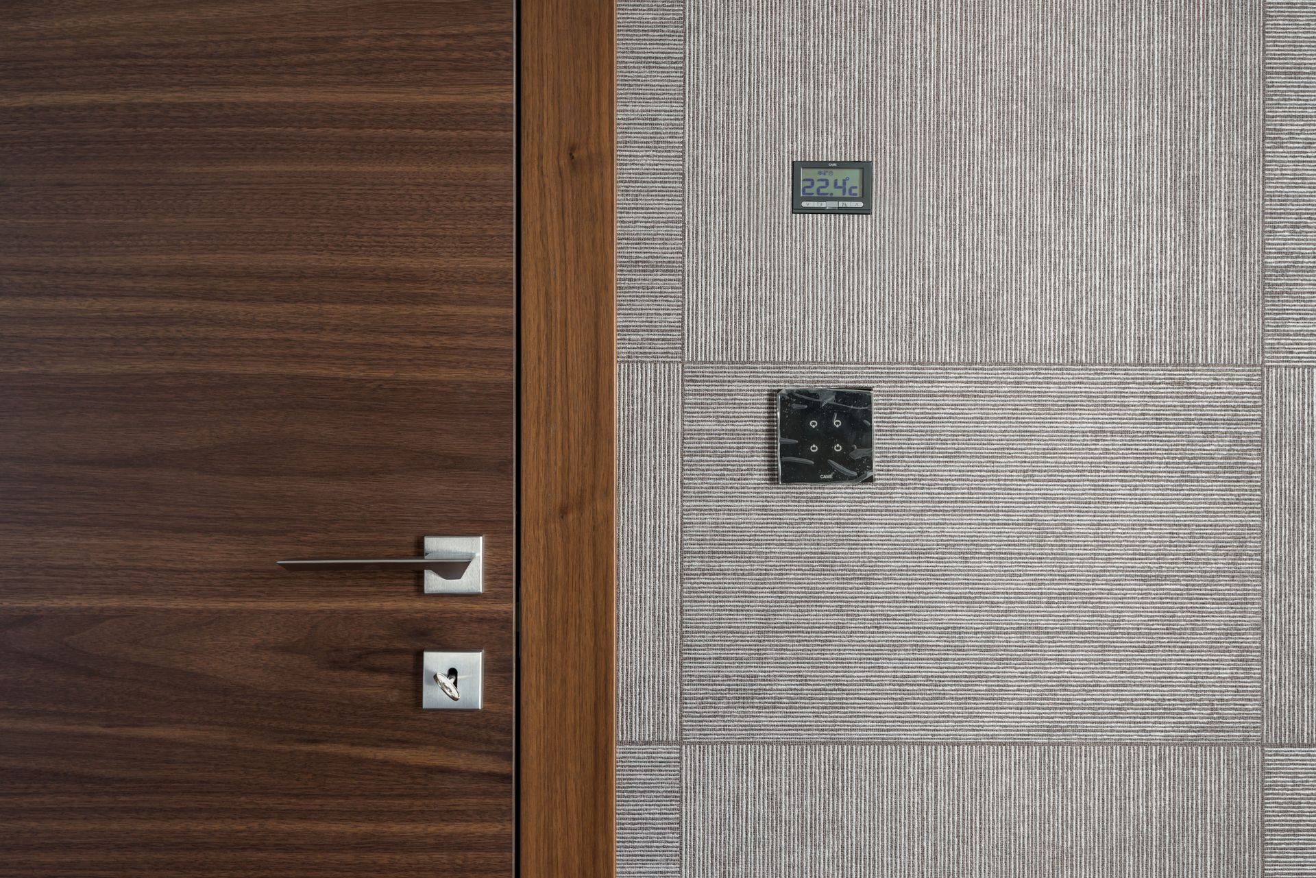 Wooden door beside a gray tiled wall with two wall switches and a small control panel.