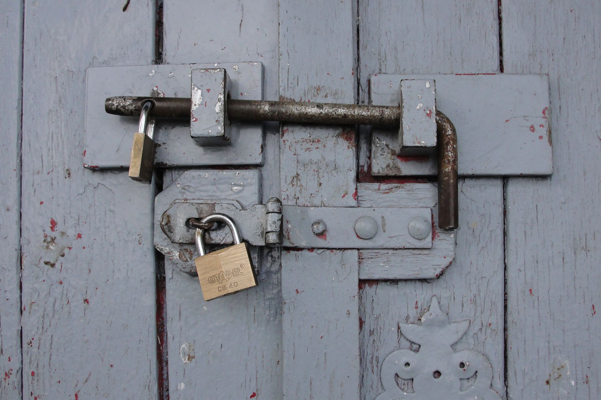 Padlock on a rusty metal latch securing a weathered gray wooden door