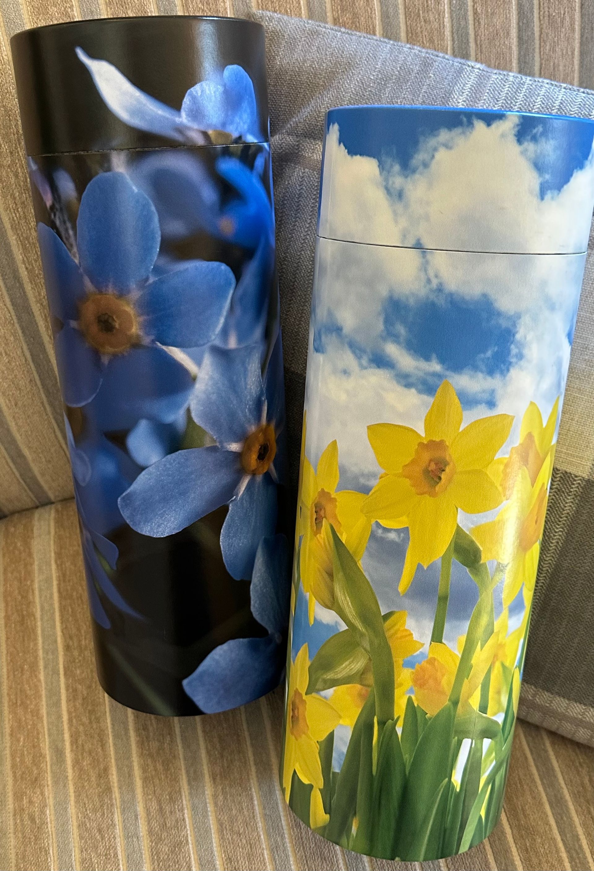 Two painted tumblers: blue flowers on black and yellow daffodils under a blue sky.