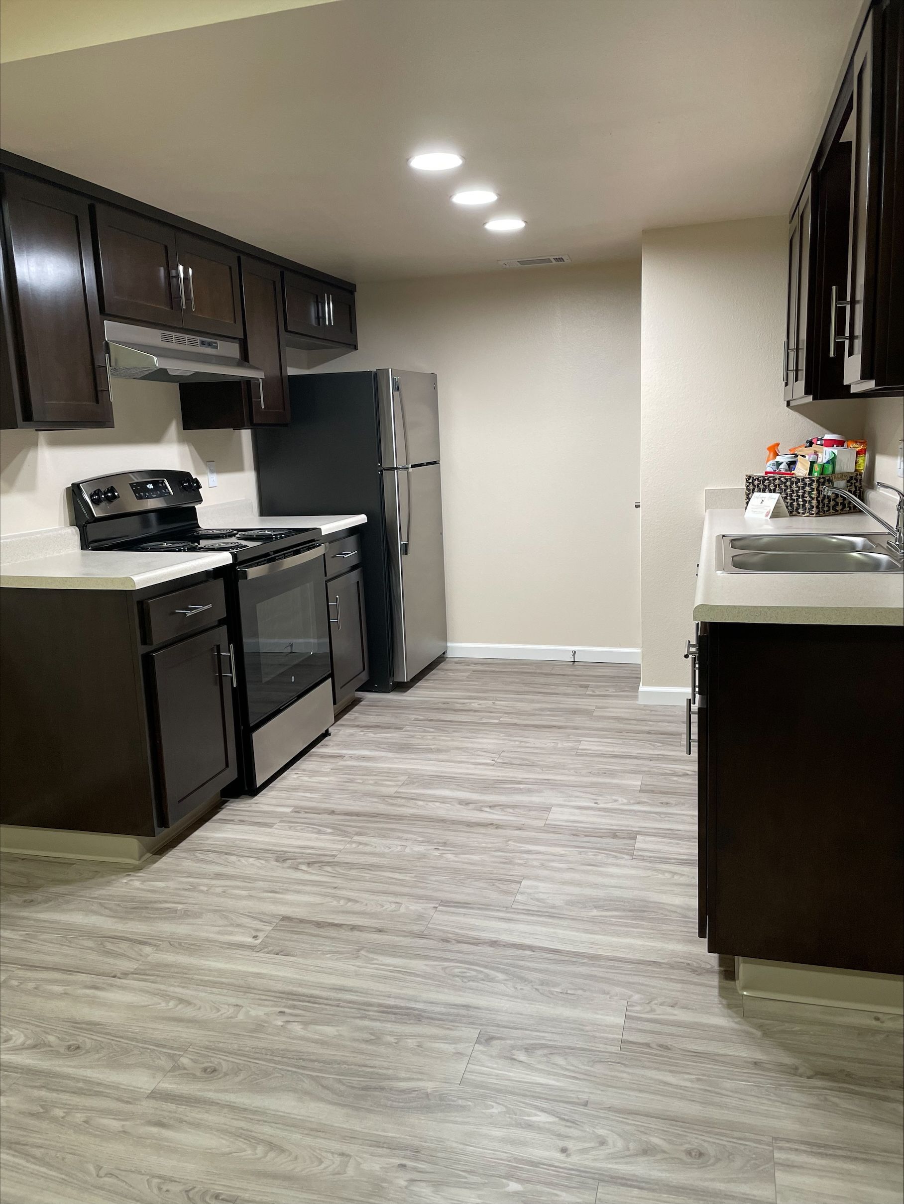 Dark brown kitchen cabinets, stainless steel appliances, gray flooring, white countertops.